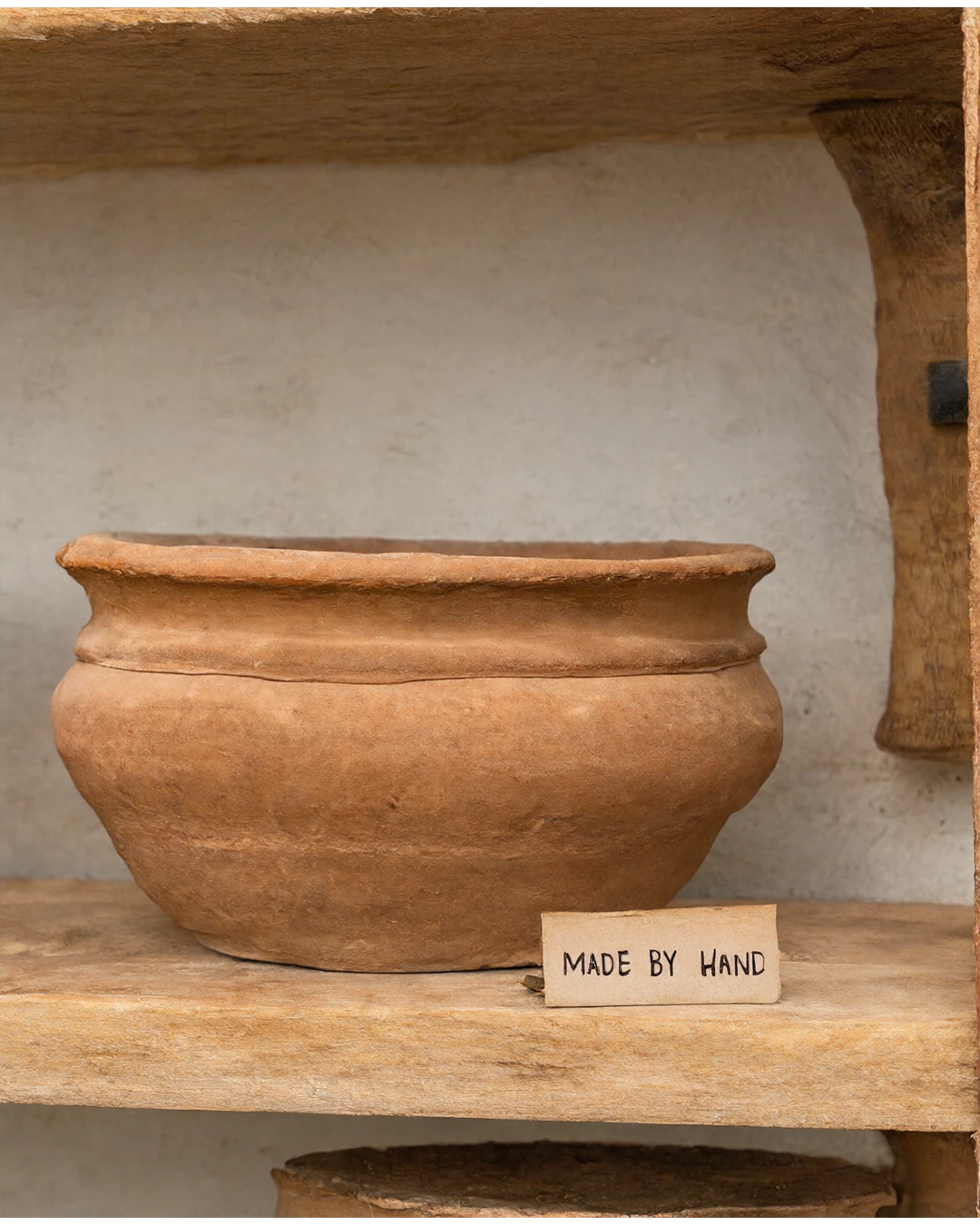 A terracotta bowl on a wooden shelf, with a clearly lettered MADE BY HAND label.